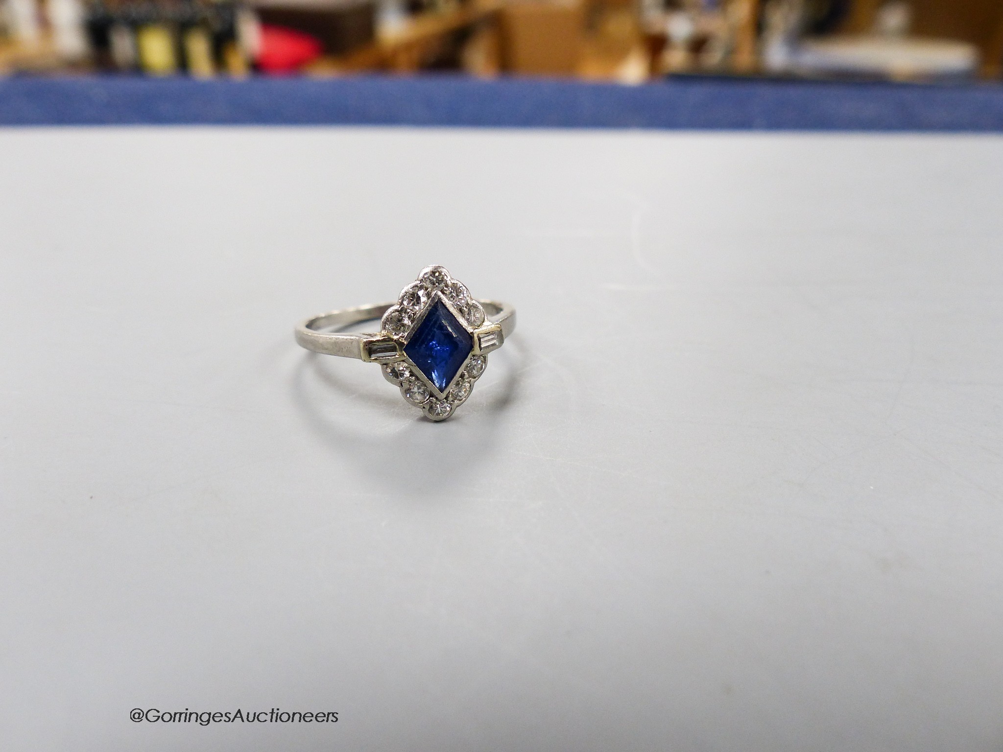 A 1920's white metal (stamped platinum), sapphire, baguette and round cut diamond cluster set lozenge shaped dress ring, size N/O, gross 3.3 grams.